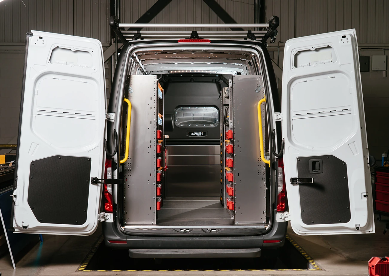 The back of an organized work van, with shelving units and drawer systems