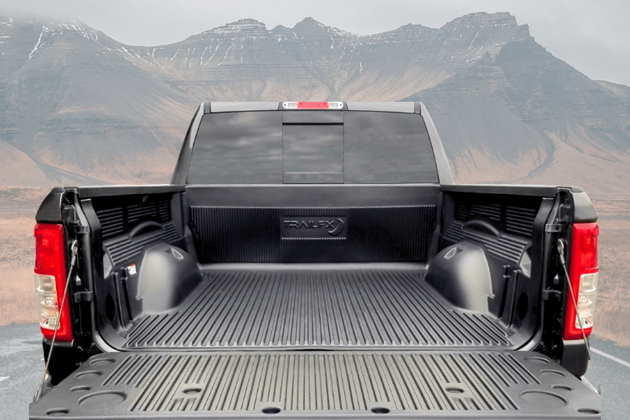 A Trail FX truck bed liner installed in the bed of black pick-up truck, against a road background