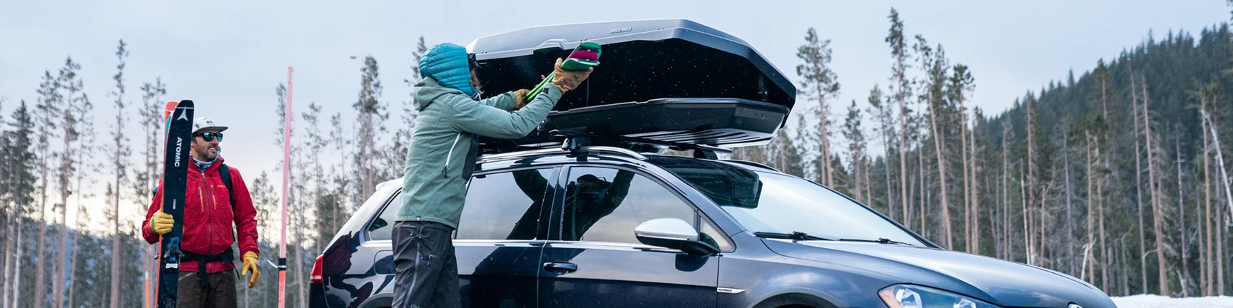 Two men unloading skis and snowboards from a Yakima rooftop cargo box, Winter Sports Racks and Cargo Carriers, Ski and Snowboard Racks, Enclosed Cargo Carriers