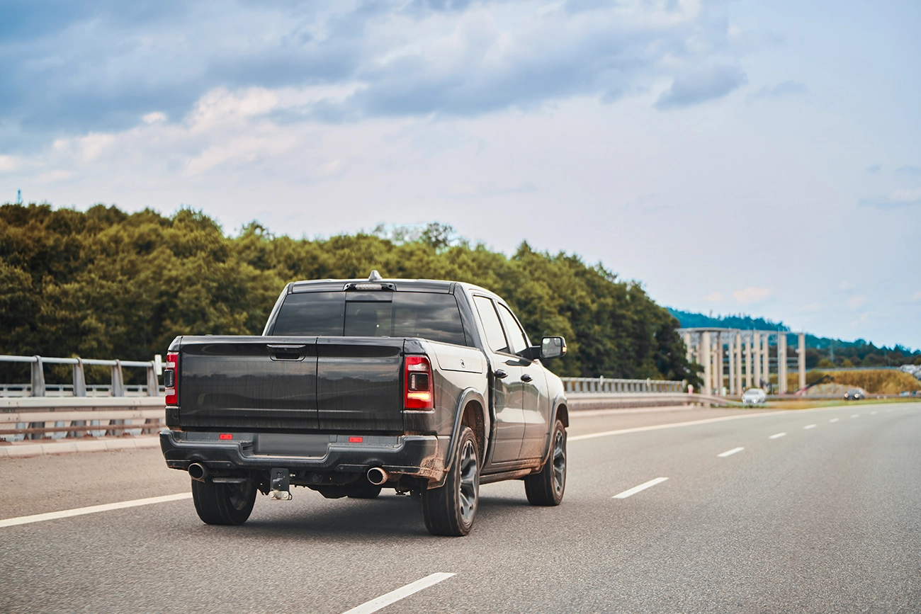 A dark gray pickup truck driving on a freeway, with trees in the background