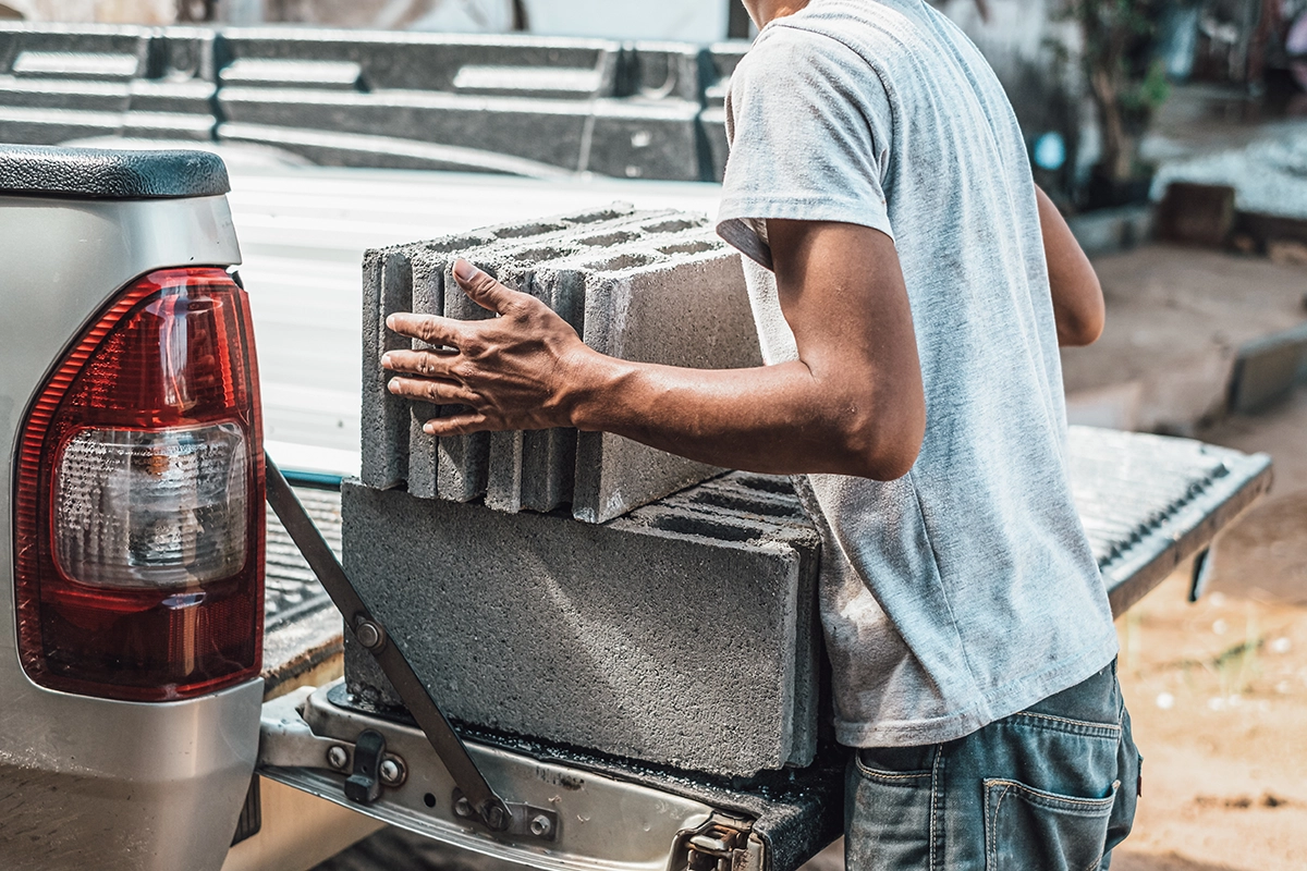 A construction worker loading cinder blocks into the back of a pickup truck