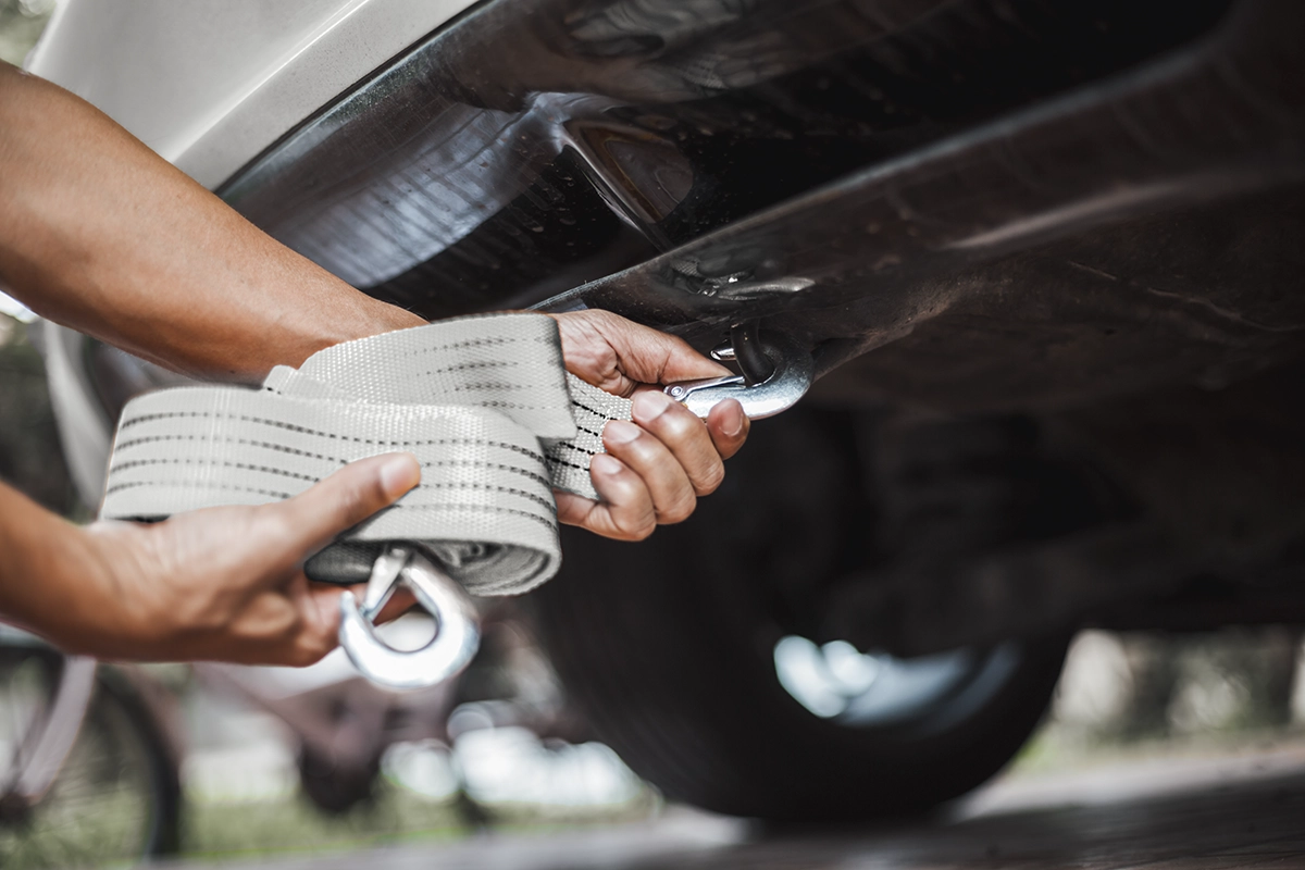 Hands attaching a gray tow strap to an off-roading vehicle, showing the concept of overlanding recovery gear