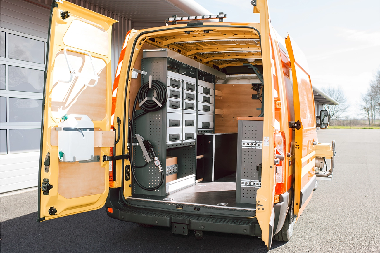 The back of an organized work van, with shelving units and drawer systems