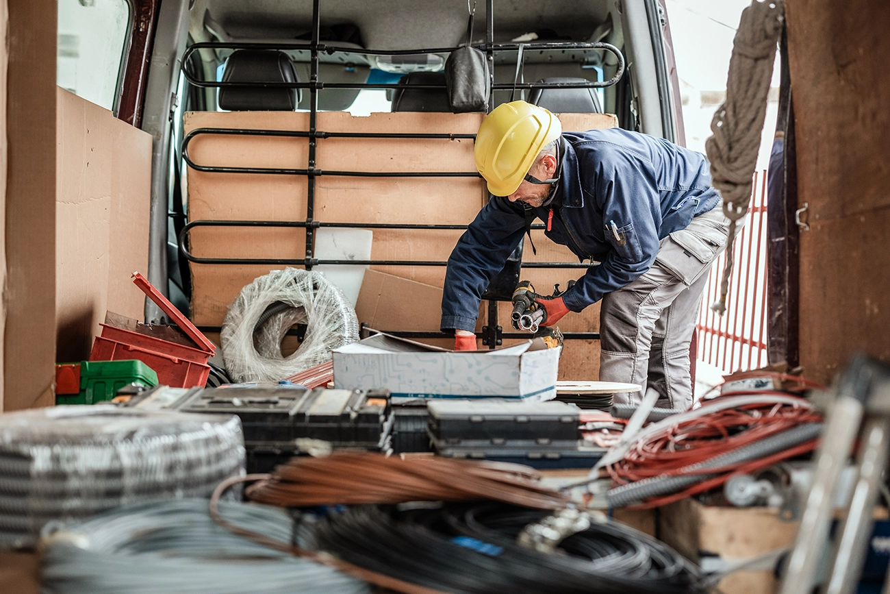 A man in a yellow hard hat organizing the back of a messy work van