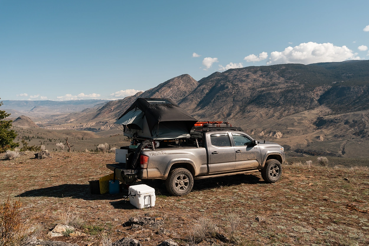 A dark grey pick-up truck, overlanding vehicle, with rooftop tent, and off-road truck accessories 