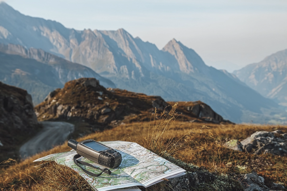 A map and an offline communicator device on the ground at a cliff overlooking mountains, showing the concept of recovery gear for overlanding and off-roading
