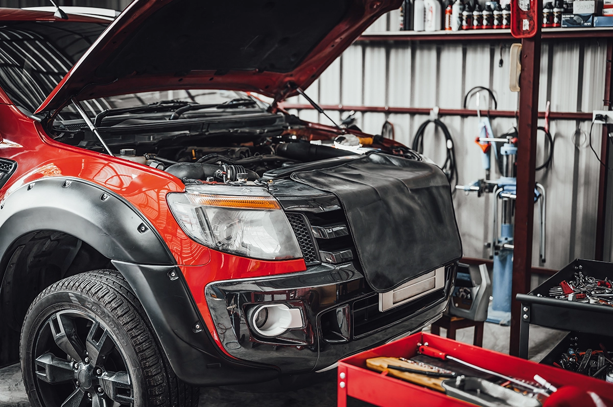 A dark red pickup truck in a shop with its hood open, revealing the engine, showing the concept of pickup truck maintenance