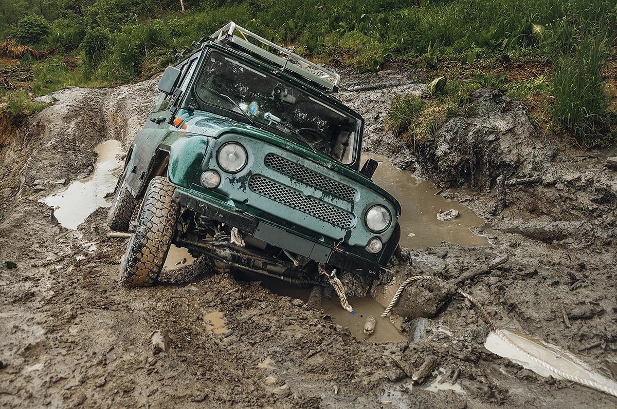 A teal overlanding vehicle stuck in the mud with trees in the background, showing the concept of recovery gear