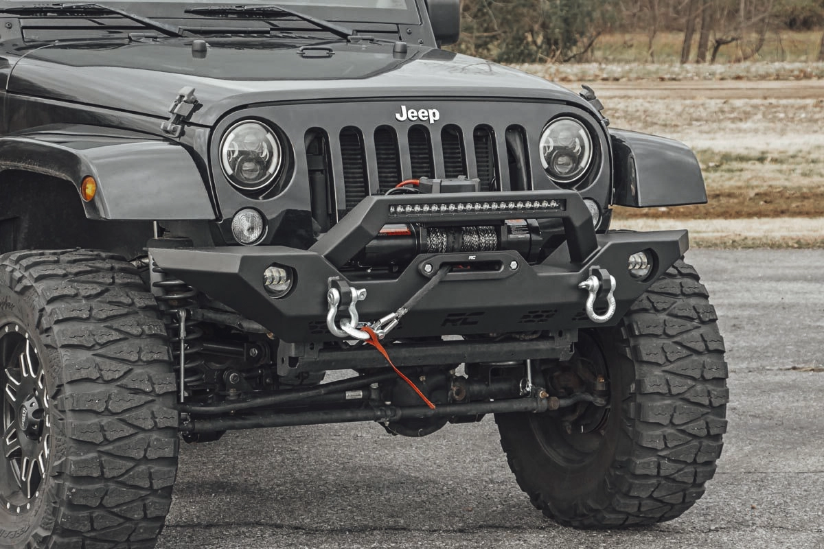 A black Jeep Wrangler with a Rough Country front winch bumper, a winch, and D-ring shackles, showing the concept of off-roading recovery gear