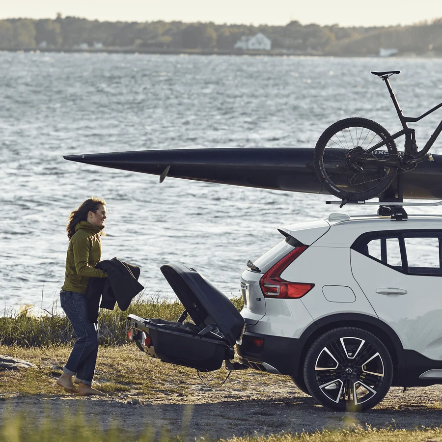 A woman loading winter sports gear into a Thule Arcos Box L hitch-mounted cargo carrier at a lake