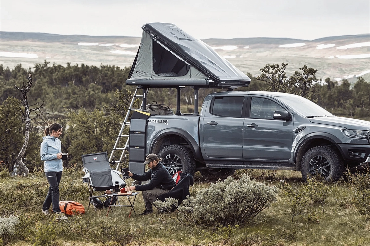 The Thule Basin Wedge hardshell rooftop tent, on a gray pickup truck, at a campsite in the grass