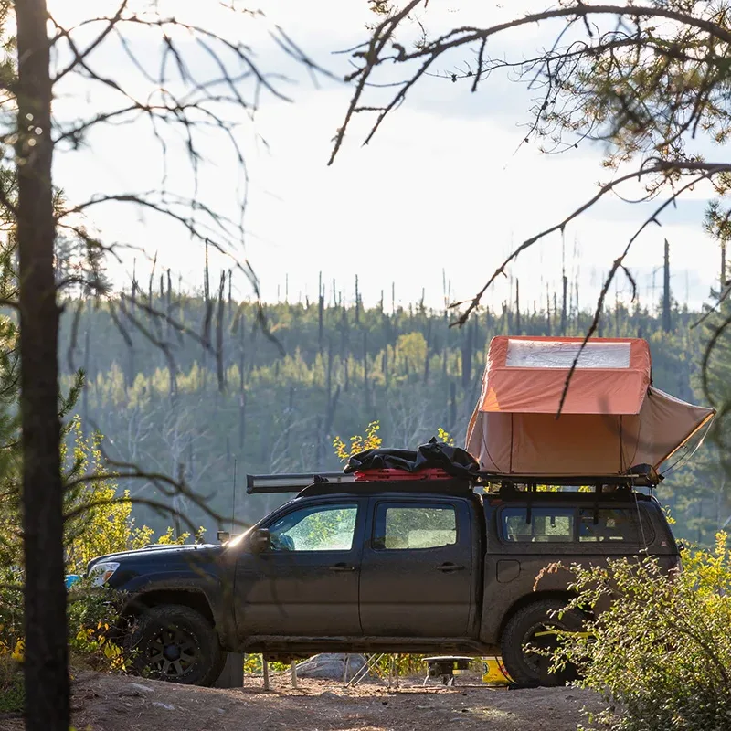 A dark gray pickup truck with a red rooftop tent in a forest, showing the concept of truck camping gear