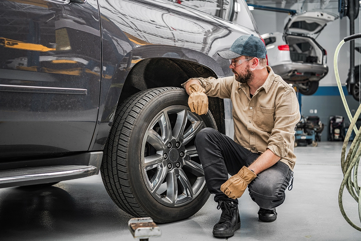 A truck mechanic crouching next to a tire, showing the concept of annual pickup truck maintenance