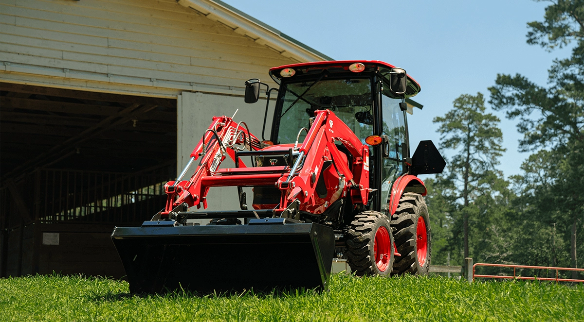 A red TYM Series 2 compact tractor in the grass in front of a shed