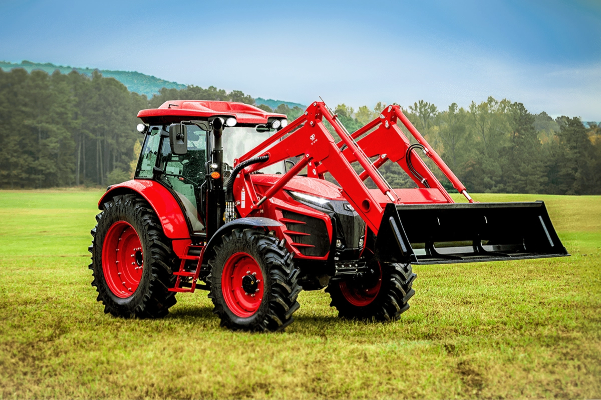 A TYM Series 6 Utility Tractor in a large field with mountains and trees in the distance