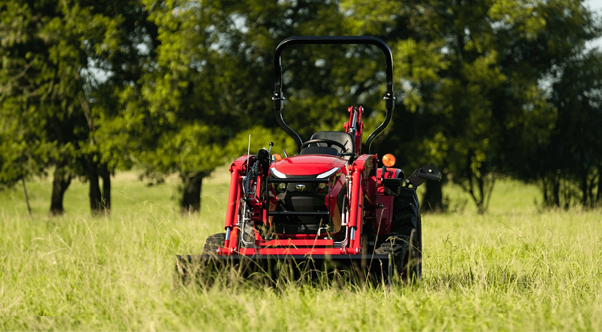 A red TYM tractor in a field of green grass, surrounded by trees