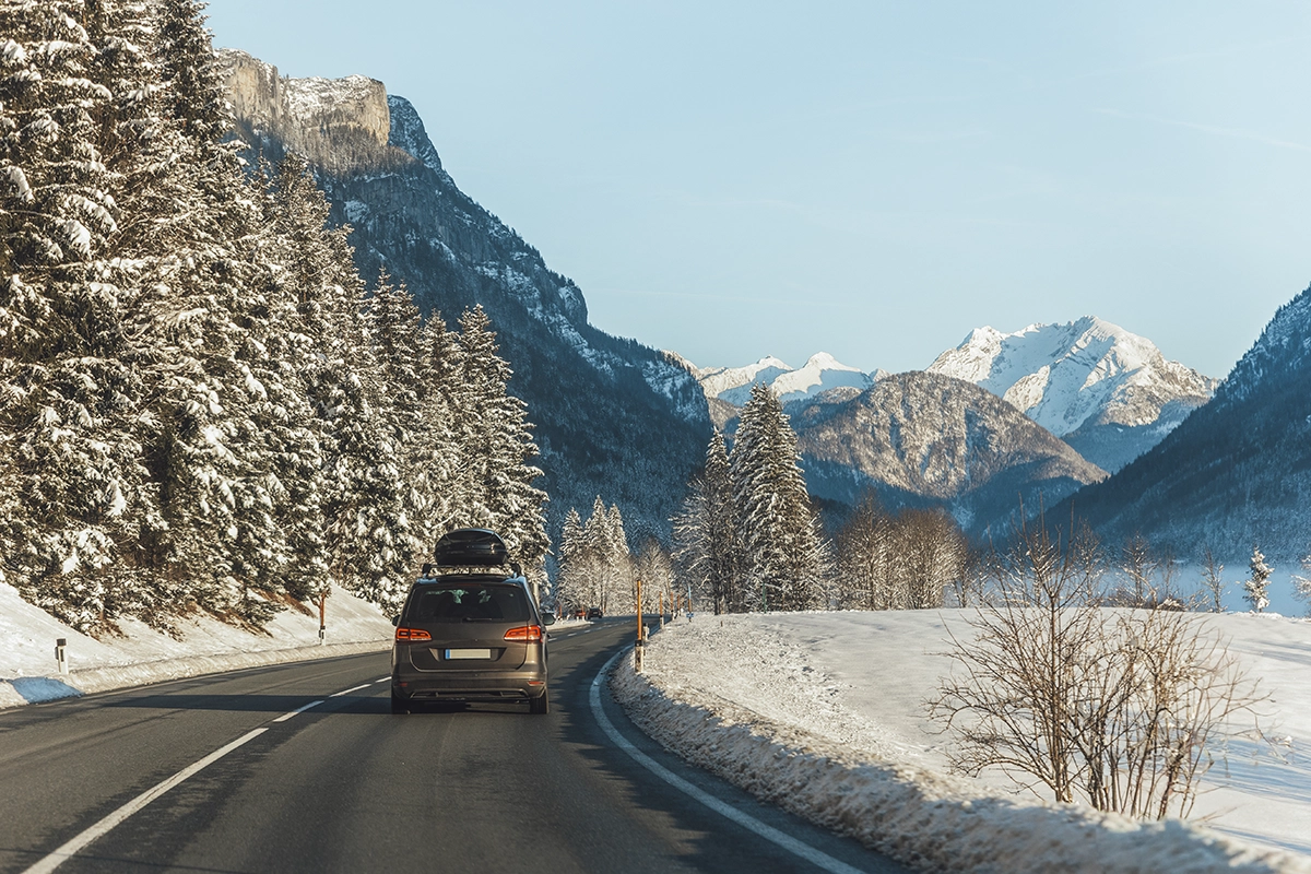 An SUV with a rooftop winter sports cargo carrier driving through snowy mountains