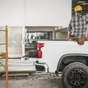 A construction worker dressed in a yellow hard hat sits in the back of a white work truck