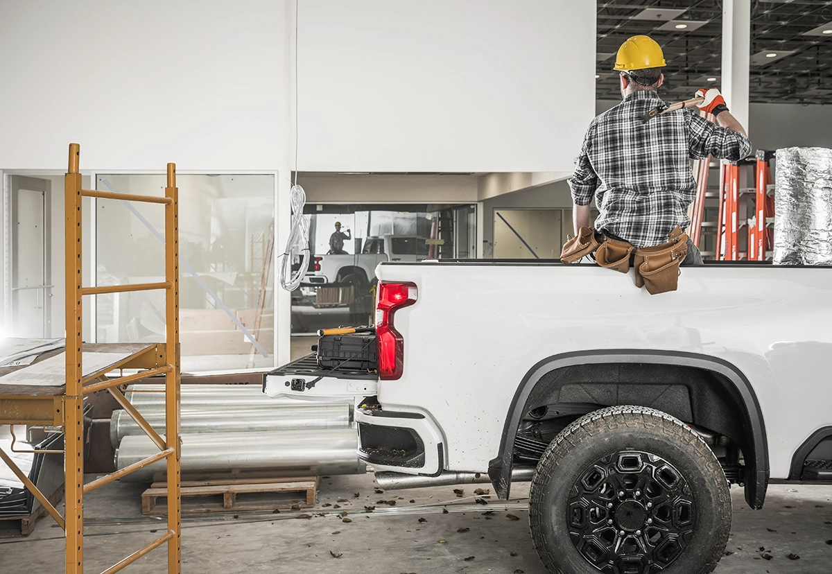 A construction worker dressed in a yellow hard hat sits in the back of a white work truck